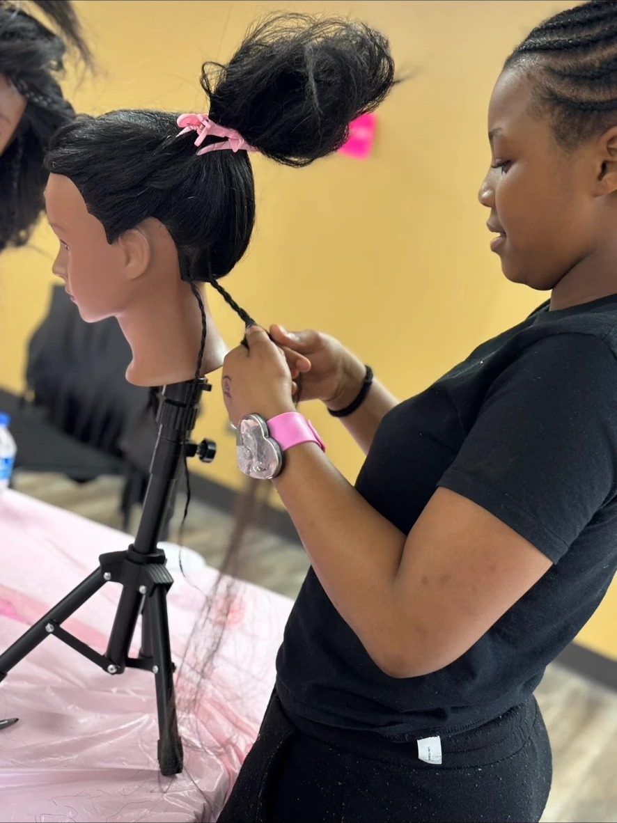 Student practicing braiding techniques on a mannequin head during a 360 Attitude youth empowerment program session